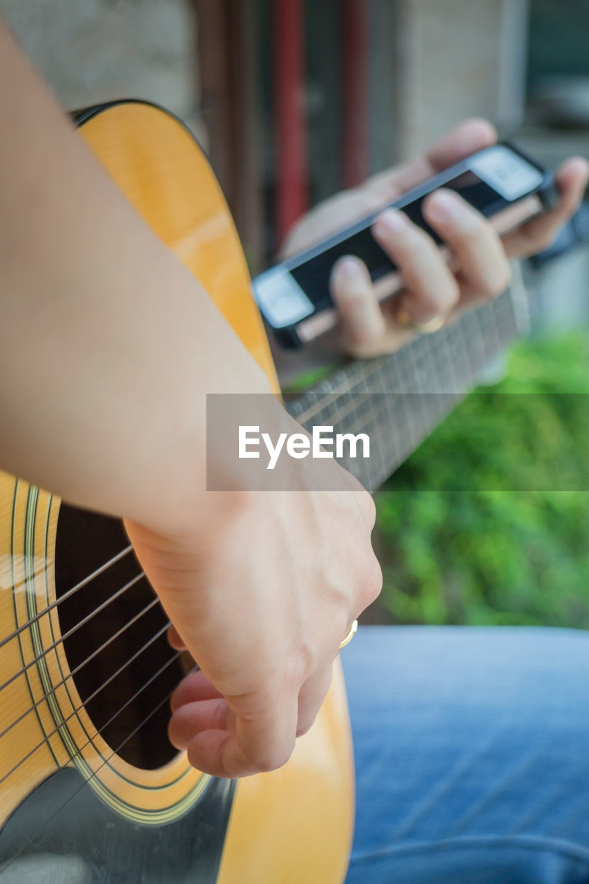 Midsection of woman playing guitar while holding mobile phone