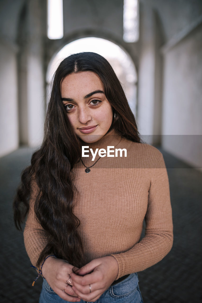 Confident teenage girl with long hair standing on footpath in tunnel