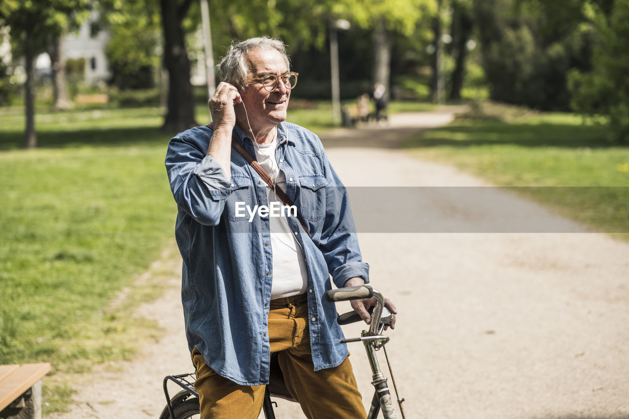 Smiling senior man wearing in-ear headphones with bicycle at park