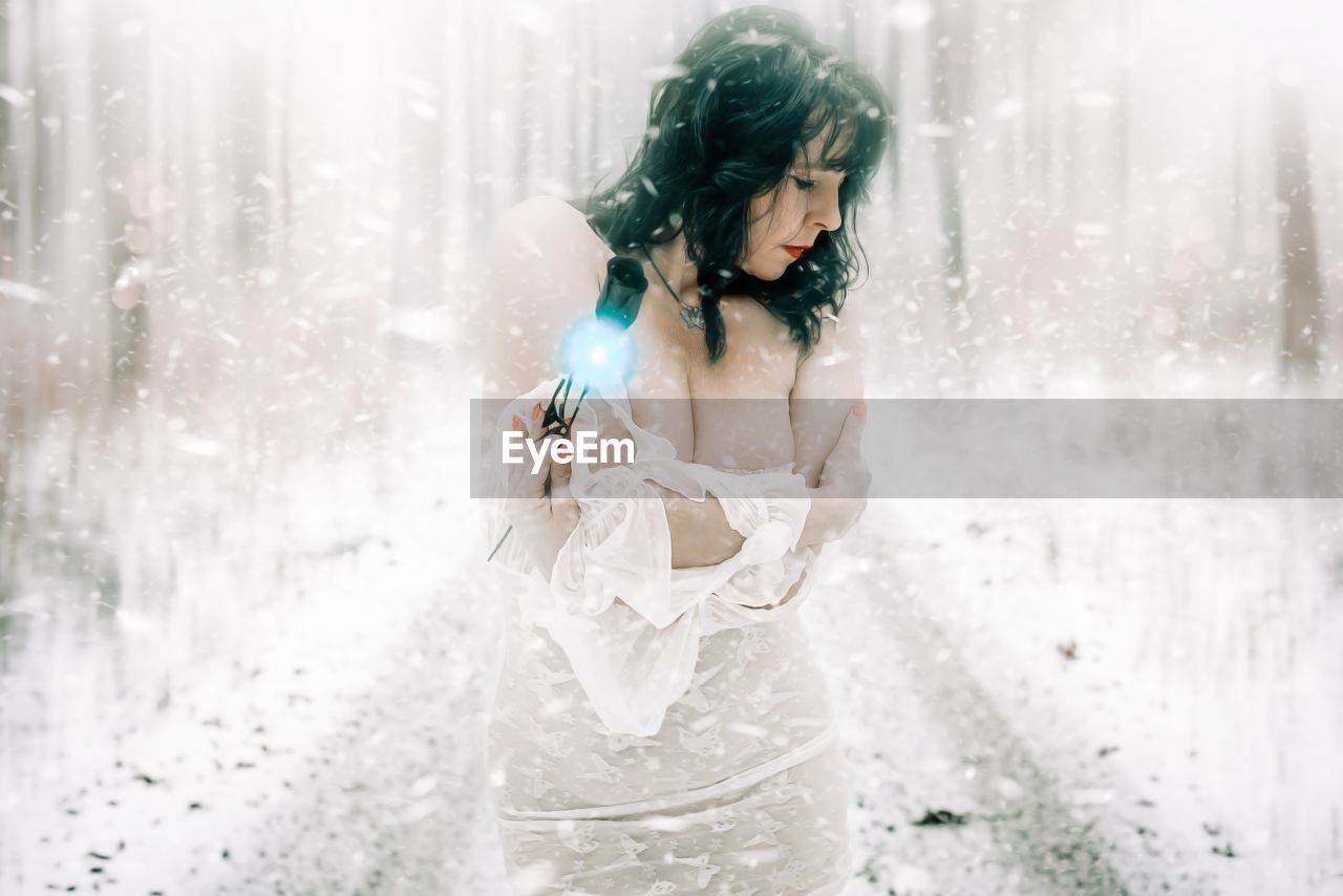 YOUNG WOMAN WITH UMBRELLA STANDING AGAINST WATER