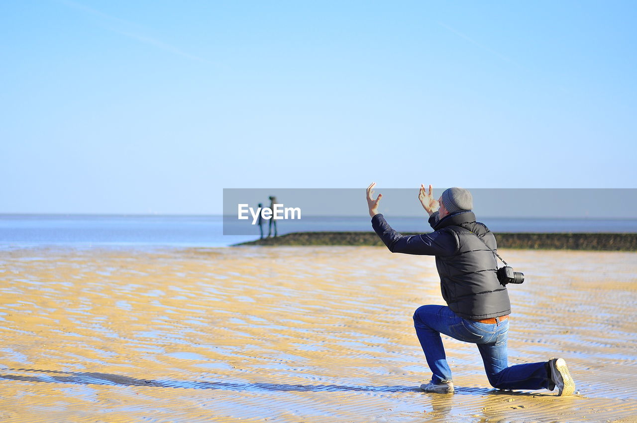 Rear view of man gesturing while kneeling at beach