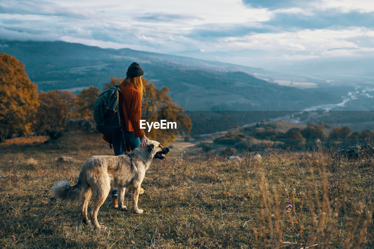 REAR VIEW OF MAN WITH DOG AGAINST MOUNTAIN