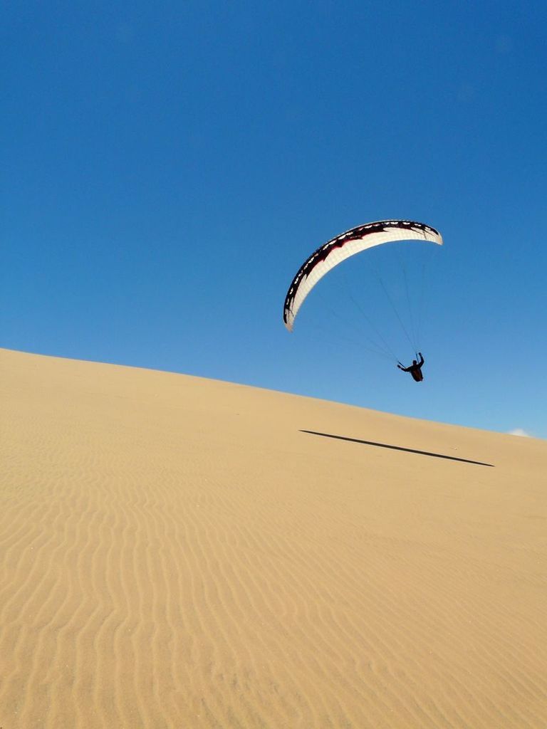 View of parachuting on desert against blue sky