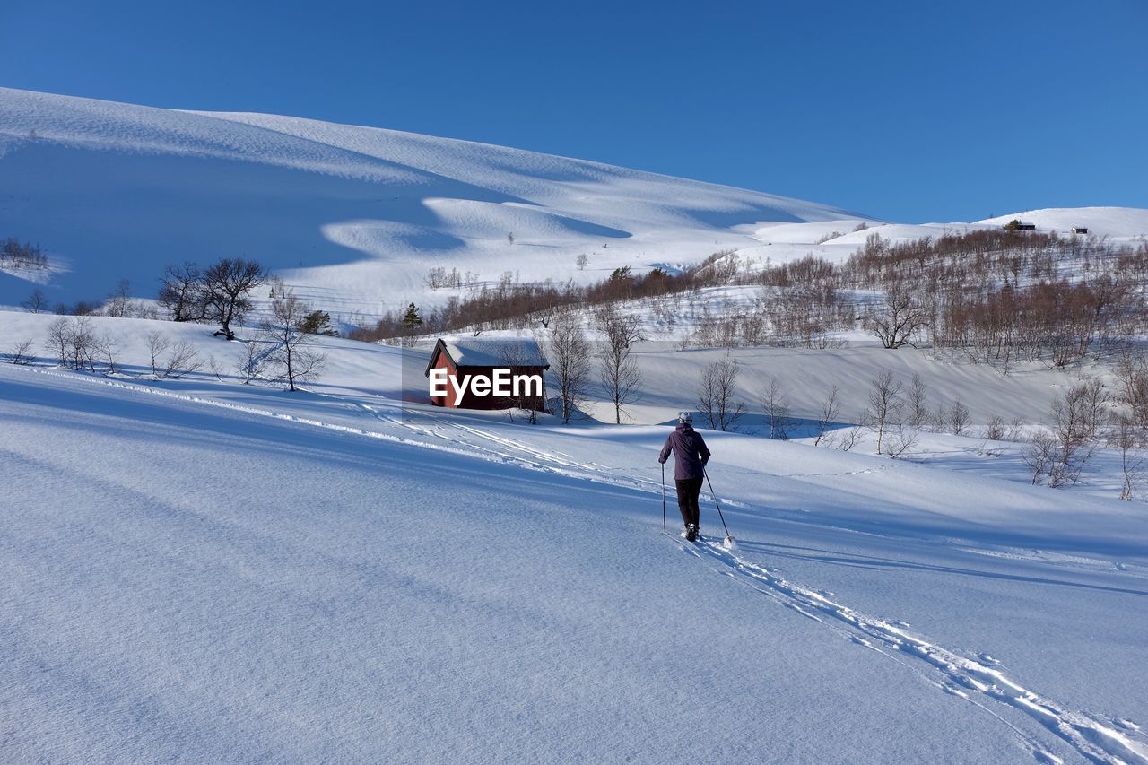 Rear view of man skiing on snow covered field against sky