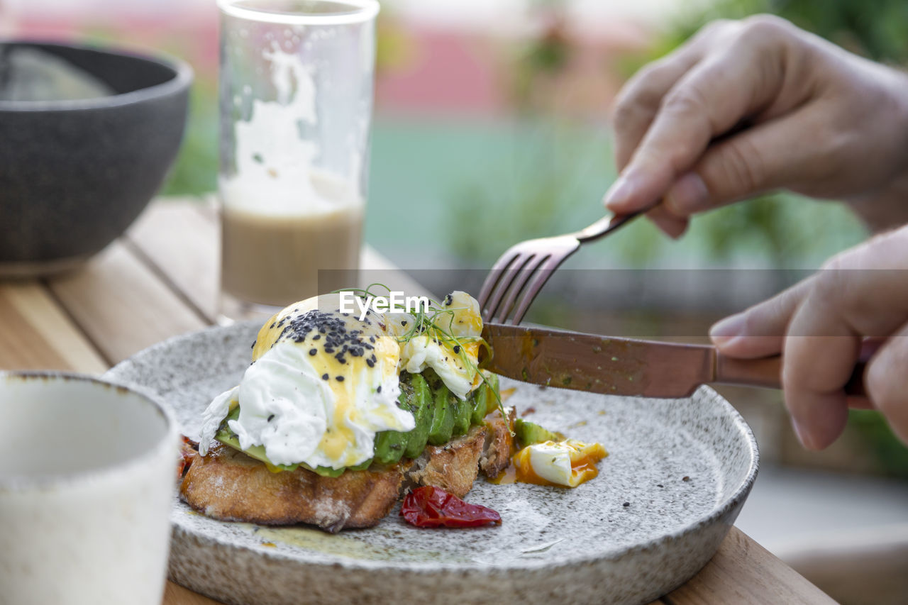 Eating poached eggs and avocado toast on the plate, hands in frame, healthy breakfast option