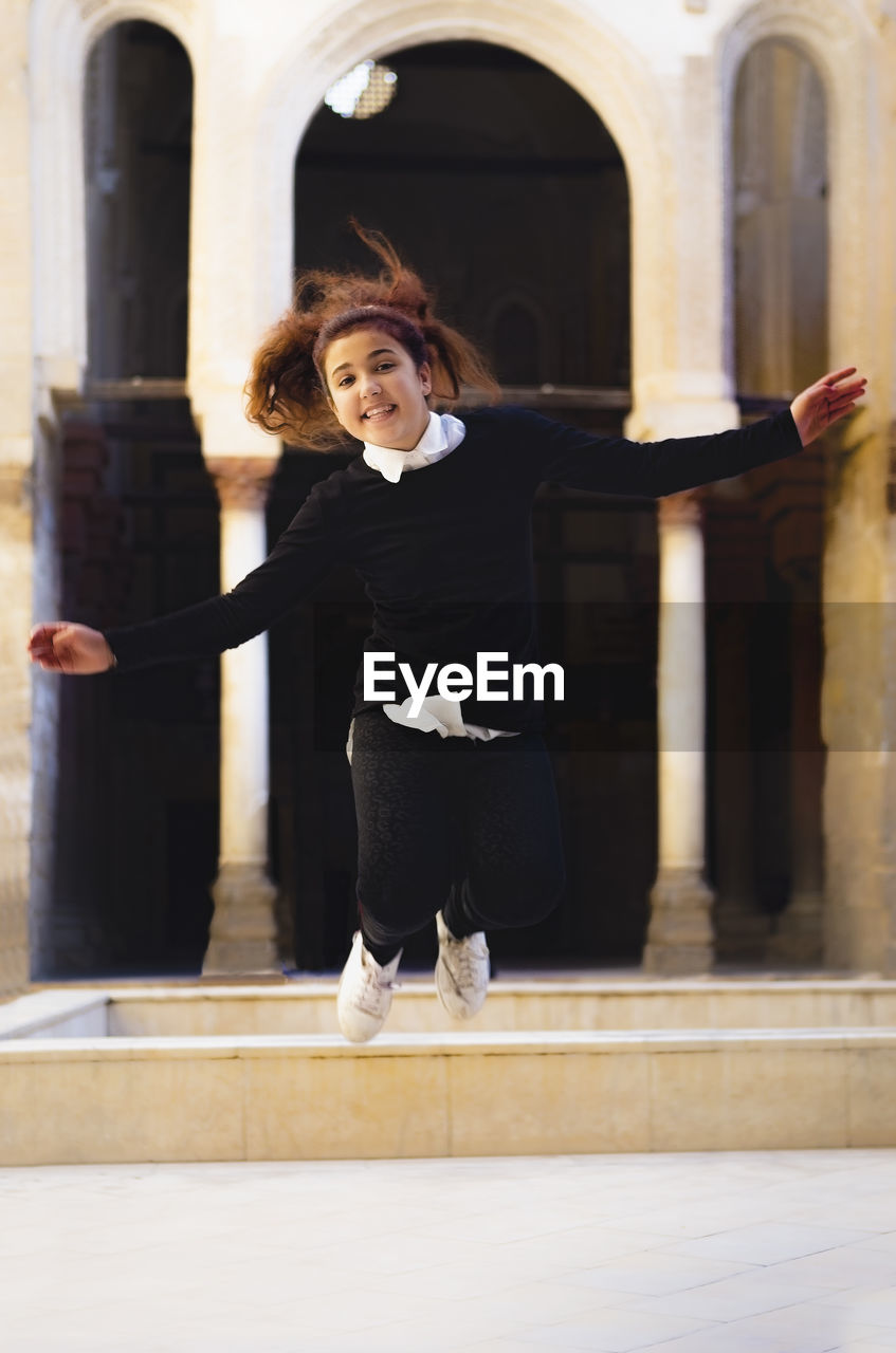 Portrait of cheerful teenage girl jumping against building