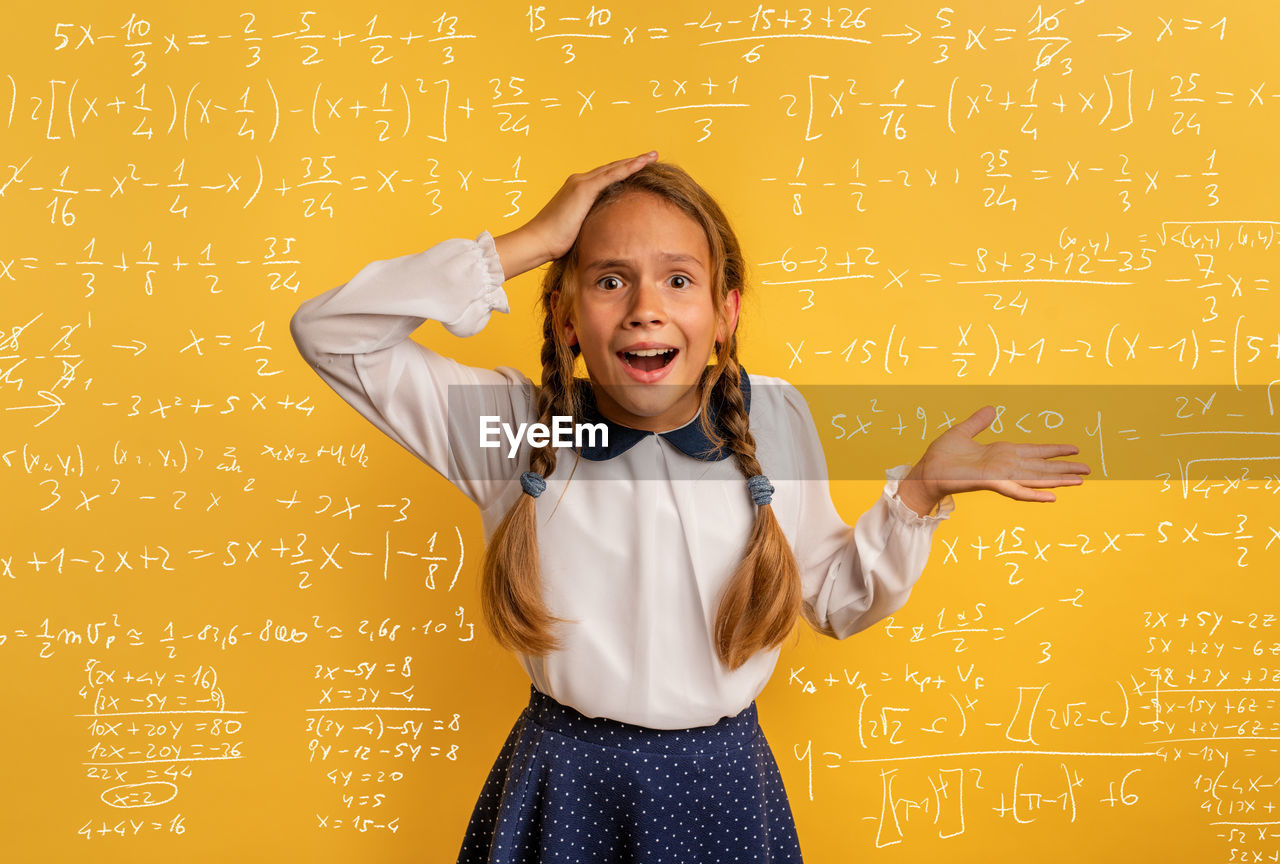 Portrait of surprised girl against mathematics on wall