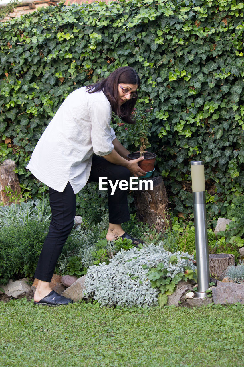 Full length of woman holding potted plant while standing by plants