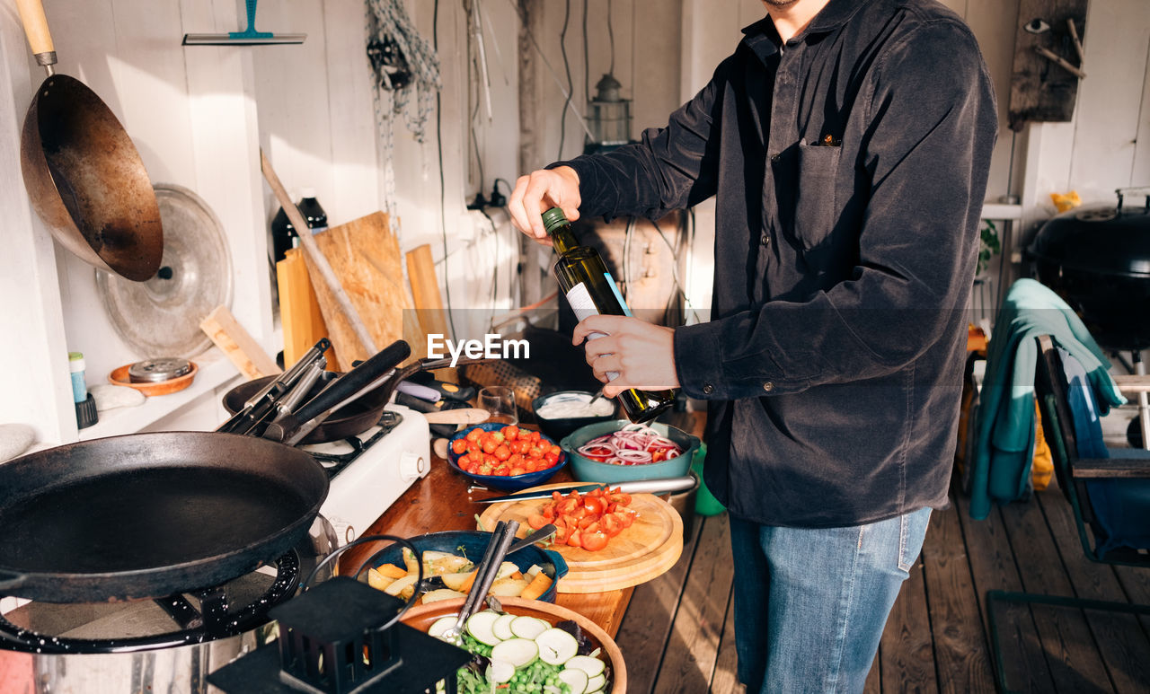 Midsection of young man holding olive oil bottle in kitchen