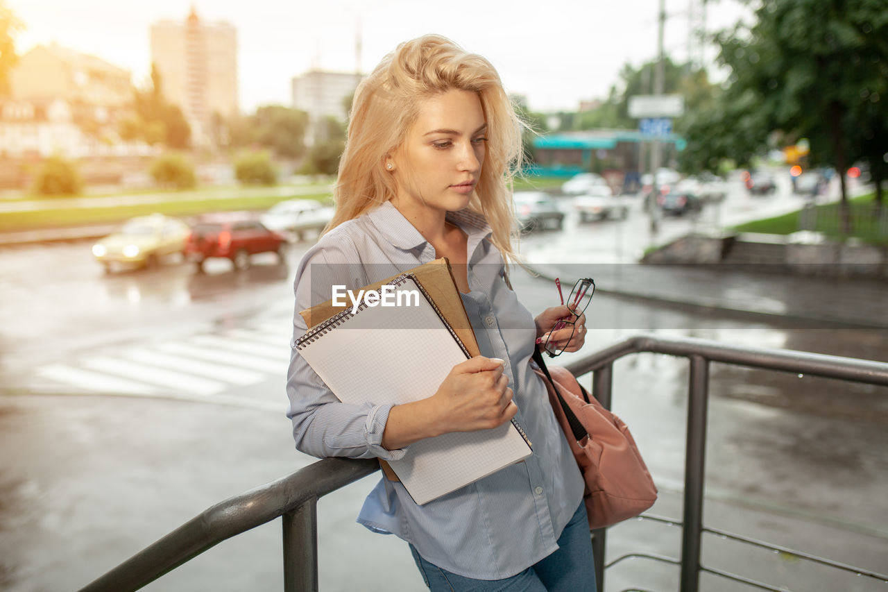 Woman with books standing at railing in city