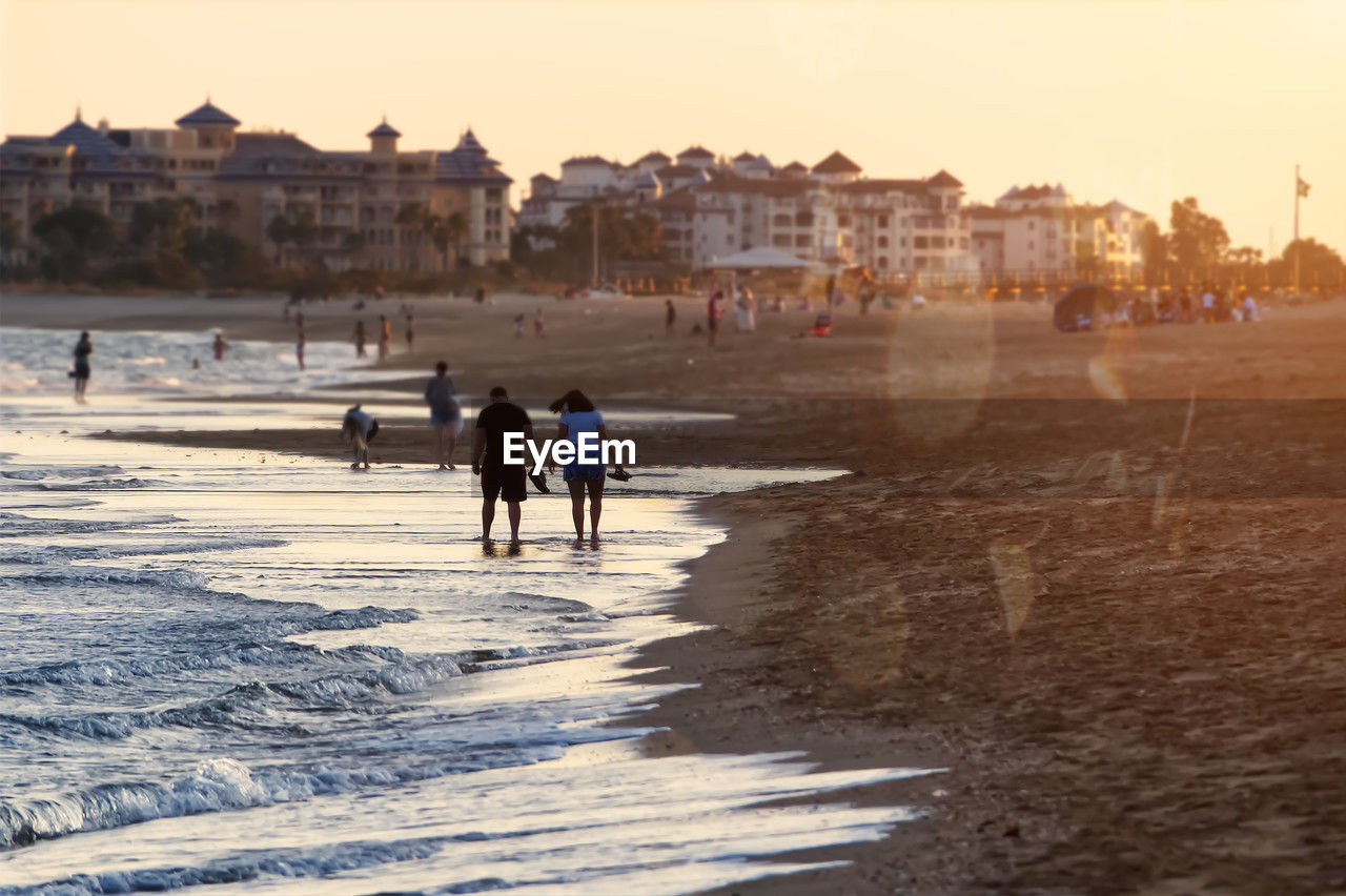 rear view of people walking on beach during sunset