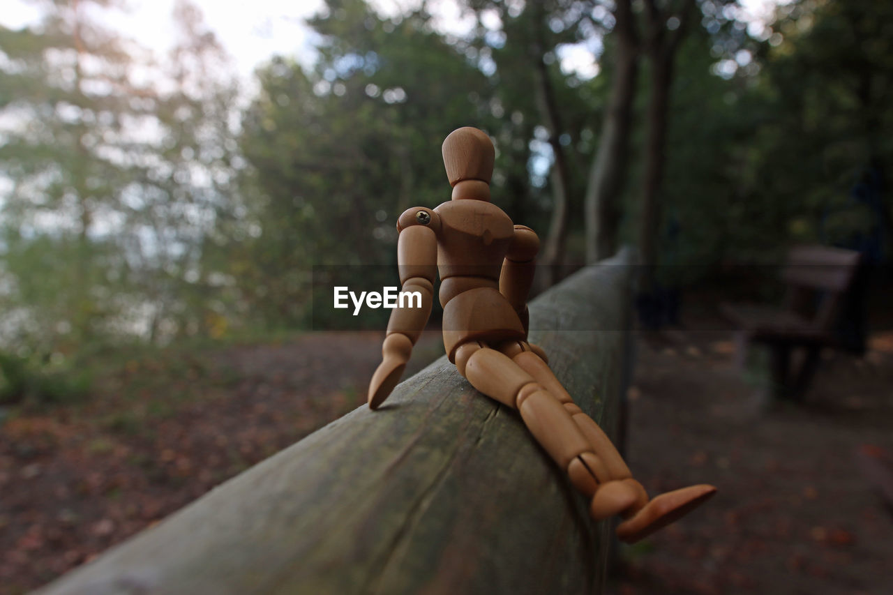 Close up along timber of a wooden mannequin sitting on a beam, relaxing in quiet lonely forest