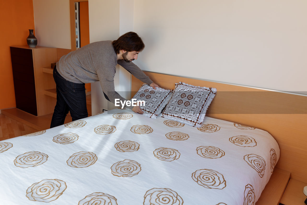 Side view of mature man arranging pillow on bed at home