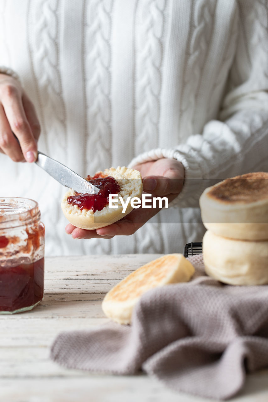 Closeup of crop person spreading yummy red berry jam on cut fresh homemade bun