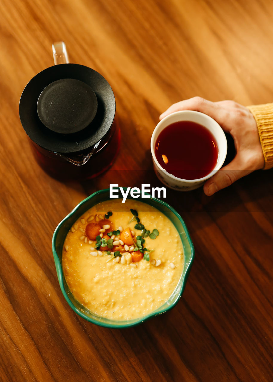 Yellow healthy pumpkin vegetarian porridge in a plate, a pot of tea and a mug on a wooden table