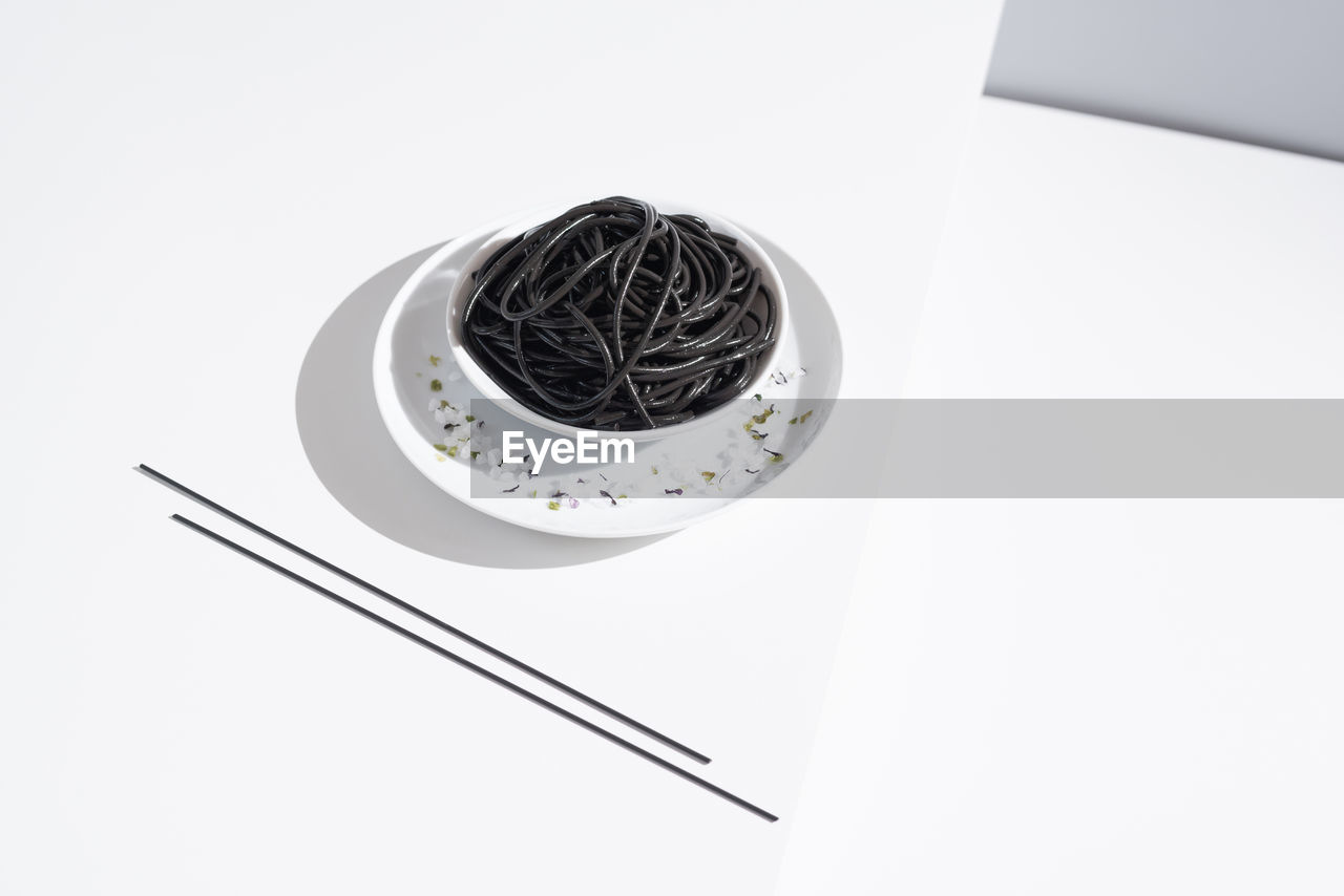 From above of ceramic bowl with delicious spaghetti with black squid ink with chopsticks on white background