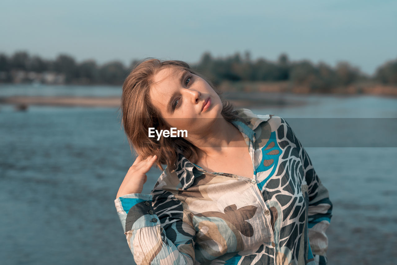 PORTRAIT OF BEAUTIFUL YOUNG WOMAN STANDING AGAINST WATER