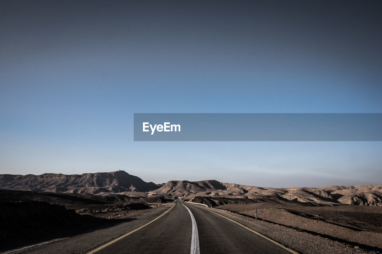 Road leading towards mountain against clear sky