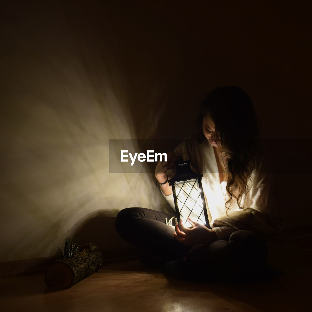 Woman holding illuminated lamp while sitting on bed at home