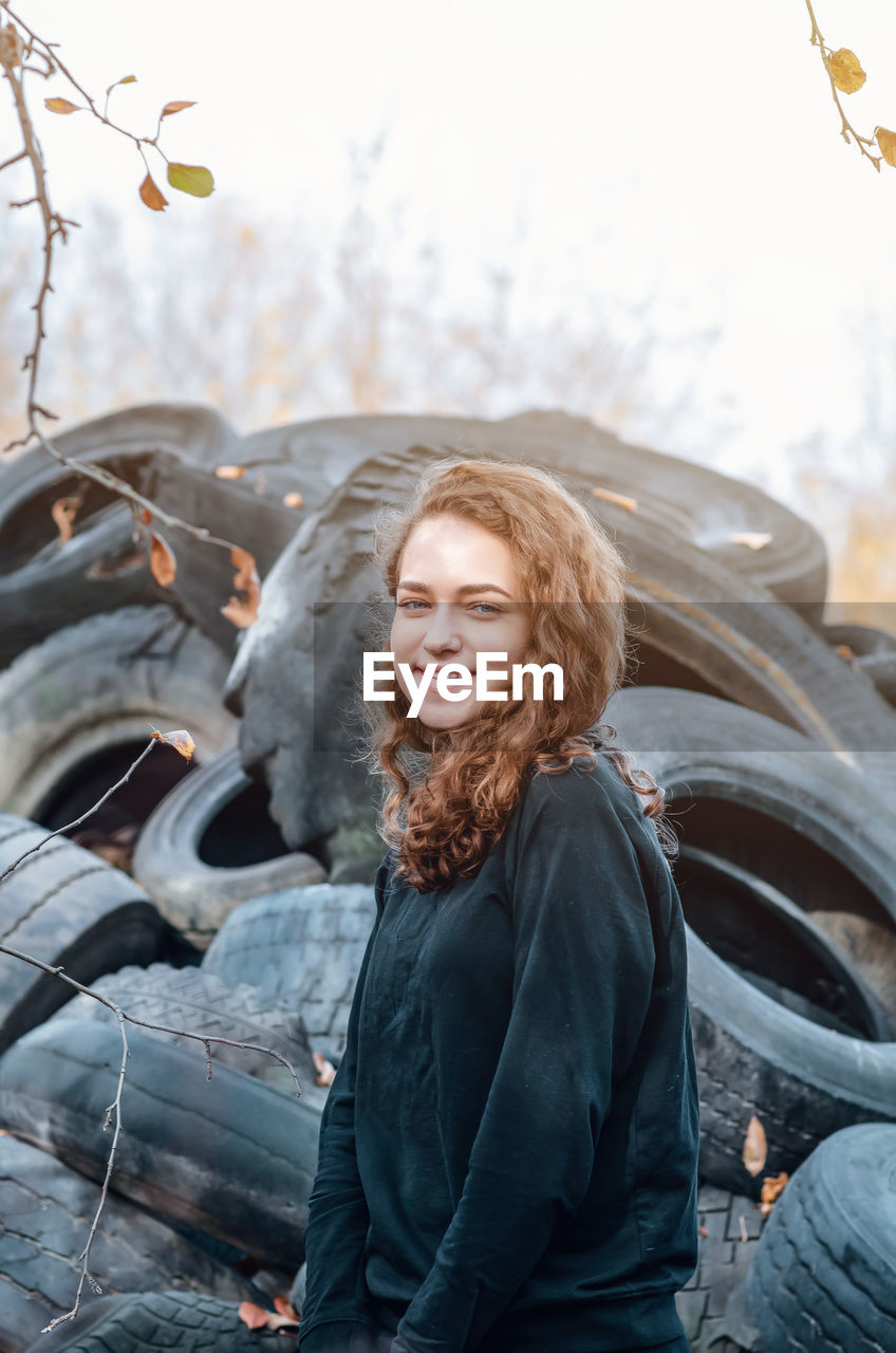 Cheerful curly-haired girl standing against a landfill of used car tires