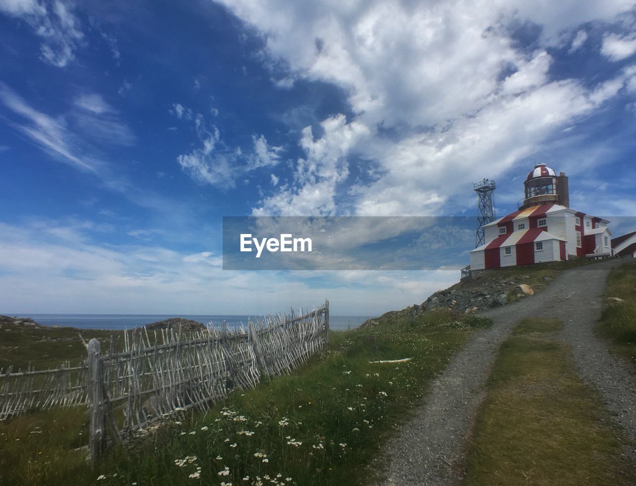 sky, cloud, architecture, hill, built structure, coast, nature, sea, tower, environment, landscape, travel destinations, building exterior, land, travel, security, building, rural area, history, protection, no people, the past, outdoors, footpath, plant, water, transportation, tourism, day, grass, road, blue, lighthouse, waterway, horizon, mountain range, scenics - nature