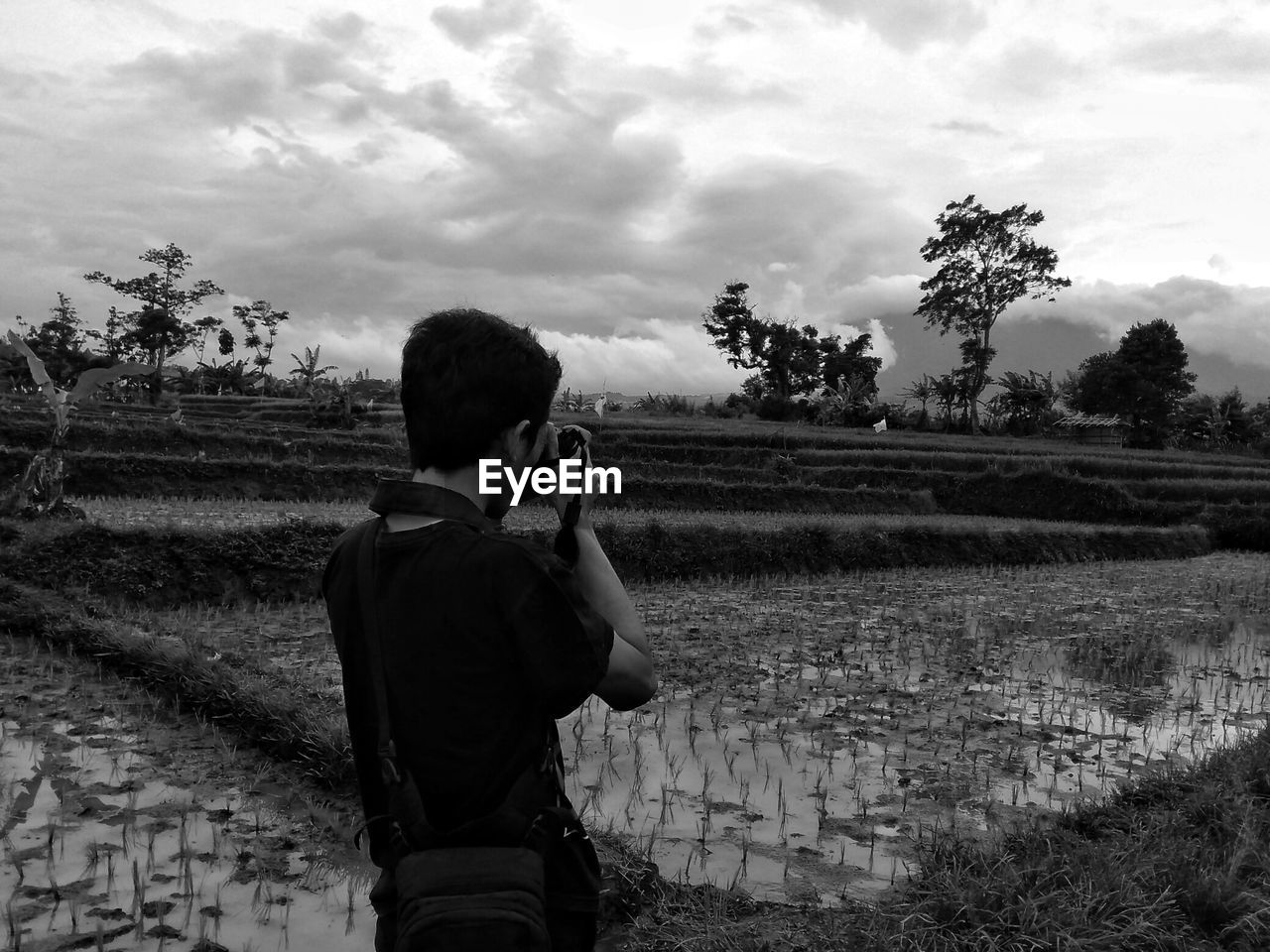 Male photographer photographing through camera while standing on field