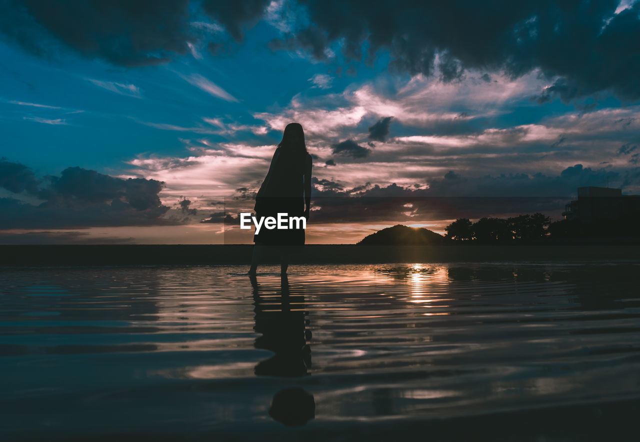 SILHOUETTE OF PERSON STANDING ON SEA SHORE DURING SUNSET