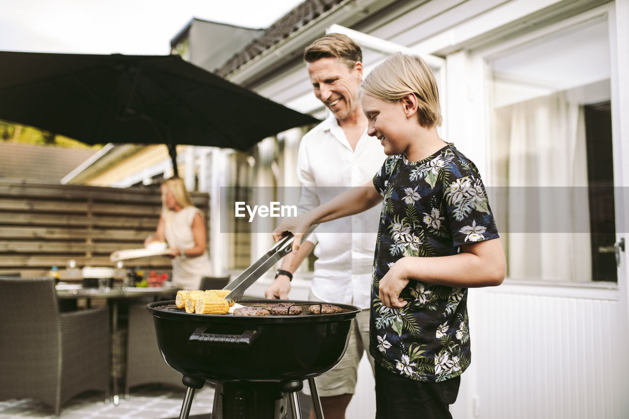 Son preparing barbecue meal with father in back yard