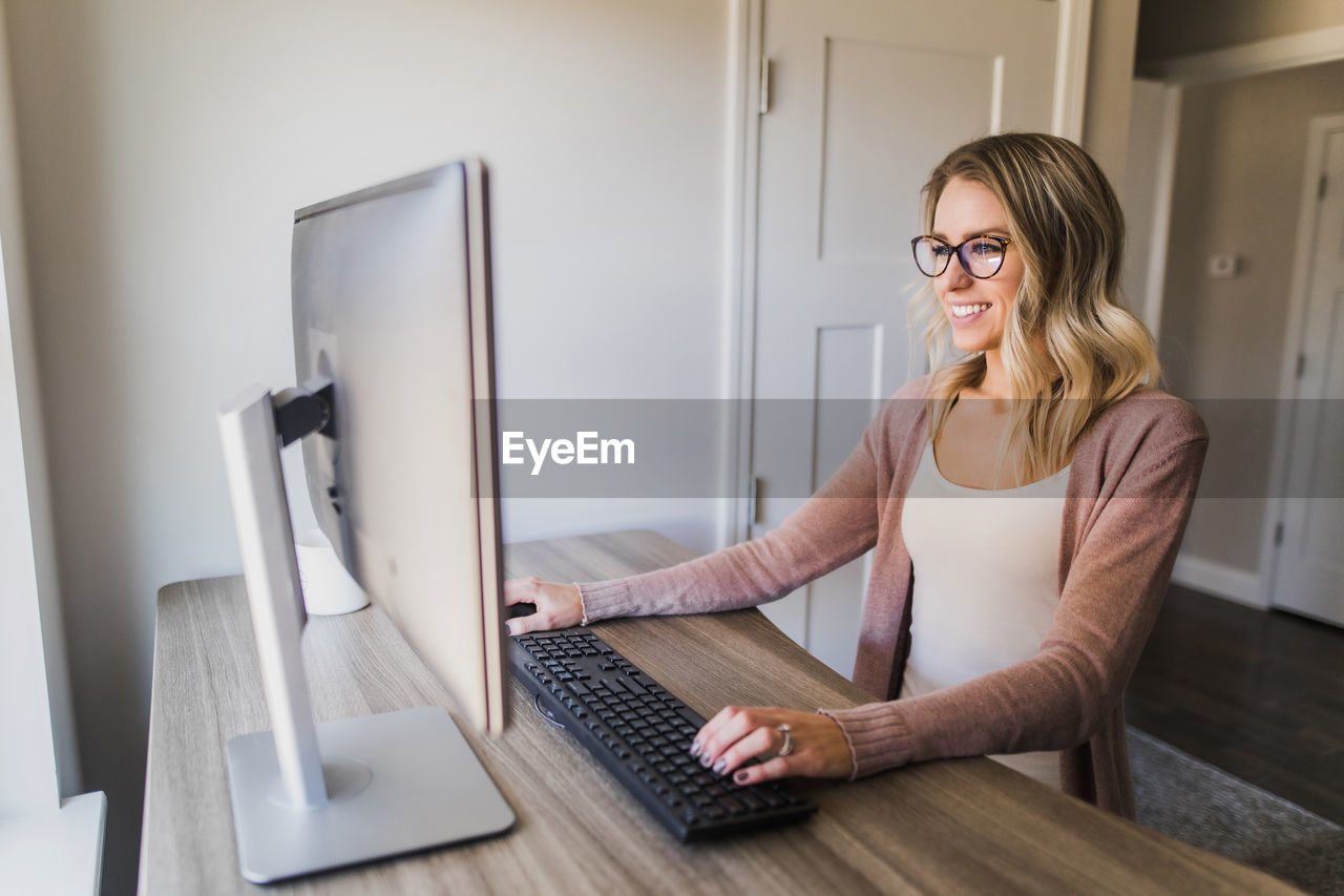 Smiling businesswoman using computer while sitting on table at home