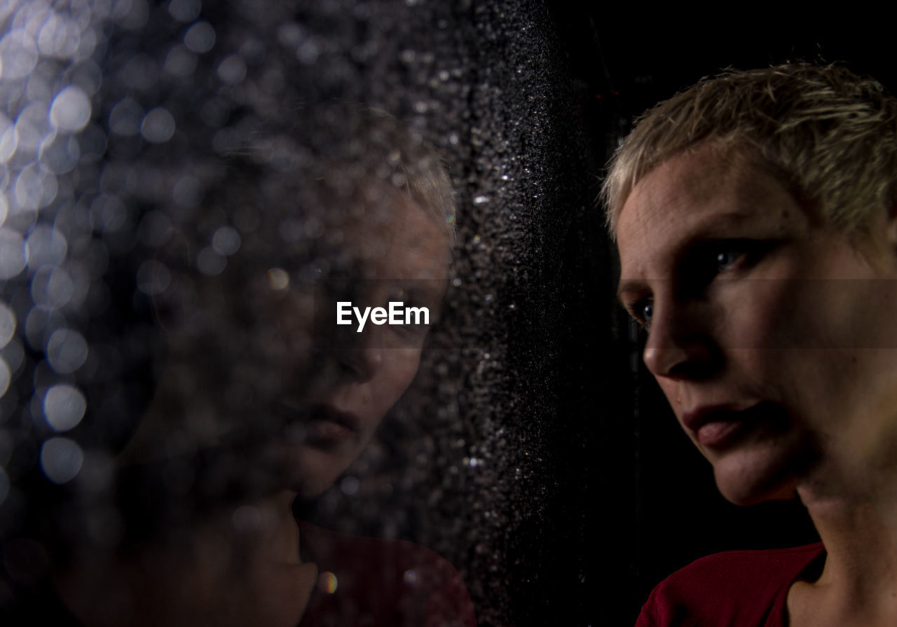 Close-up of thoughtful woman looking through wet window at night