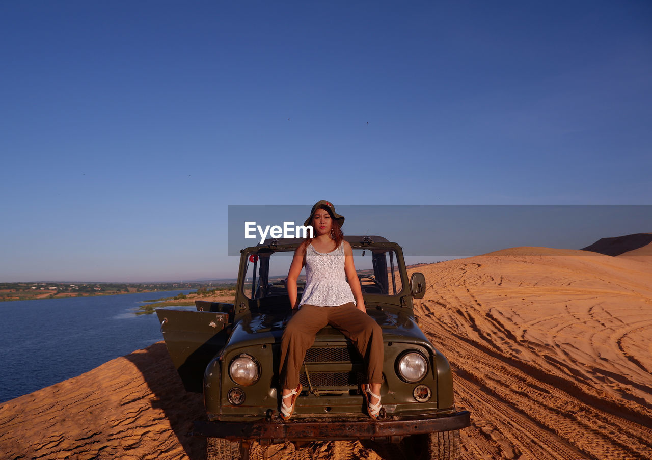 Portrait of woman sitting on off-road vehicle against clear blue sky