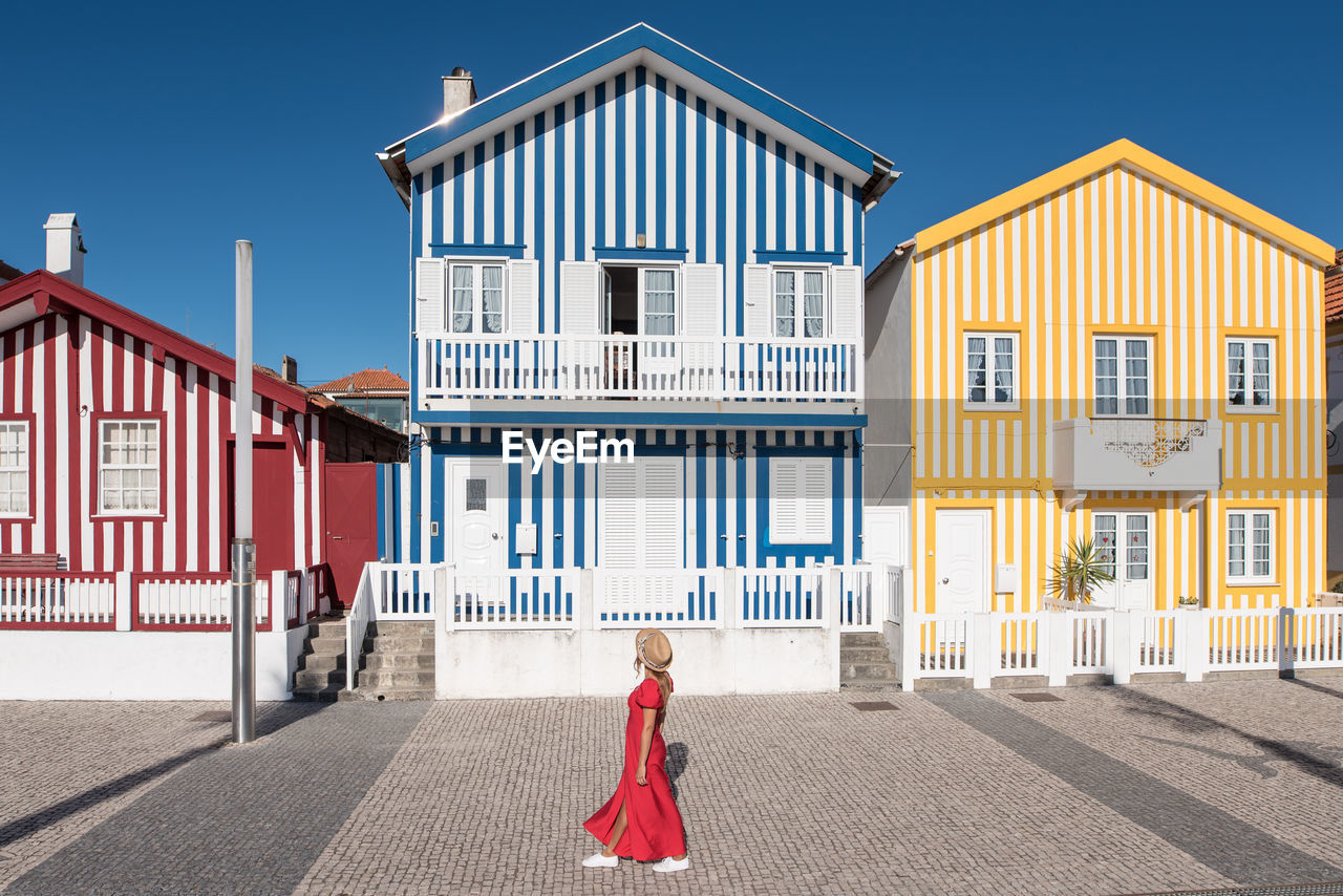 Side view of unrecognizable female tourist contemplating house exteriors with striped ornament while walking on costa nova in aveiro portugal