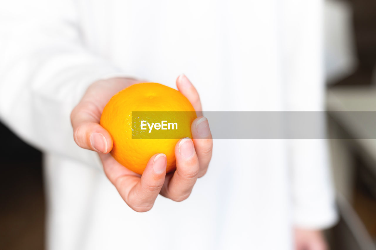 Girl in a white sweater holds a fresh sweet tangerine against the background of herself in defocus