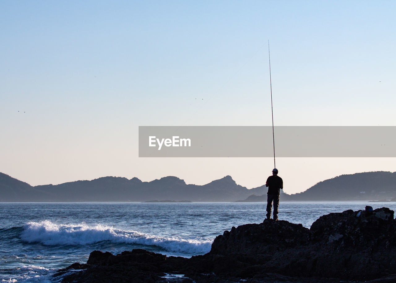 Man fishing at sea against clear sky