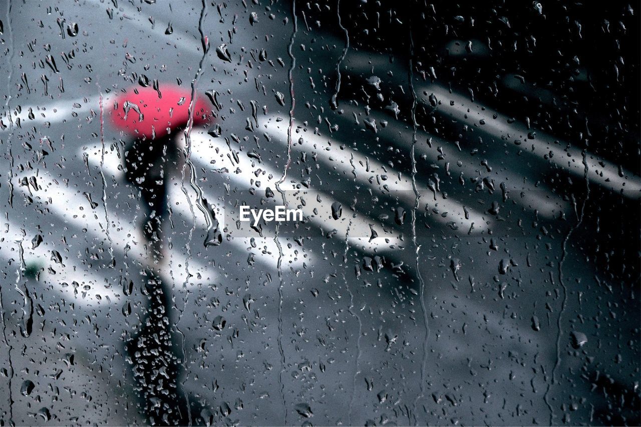 Person covering umbrella in raining season viewed through window