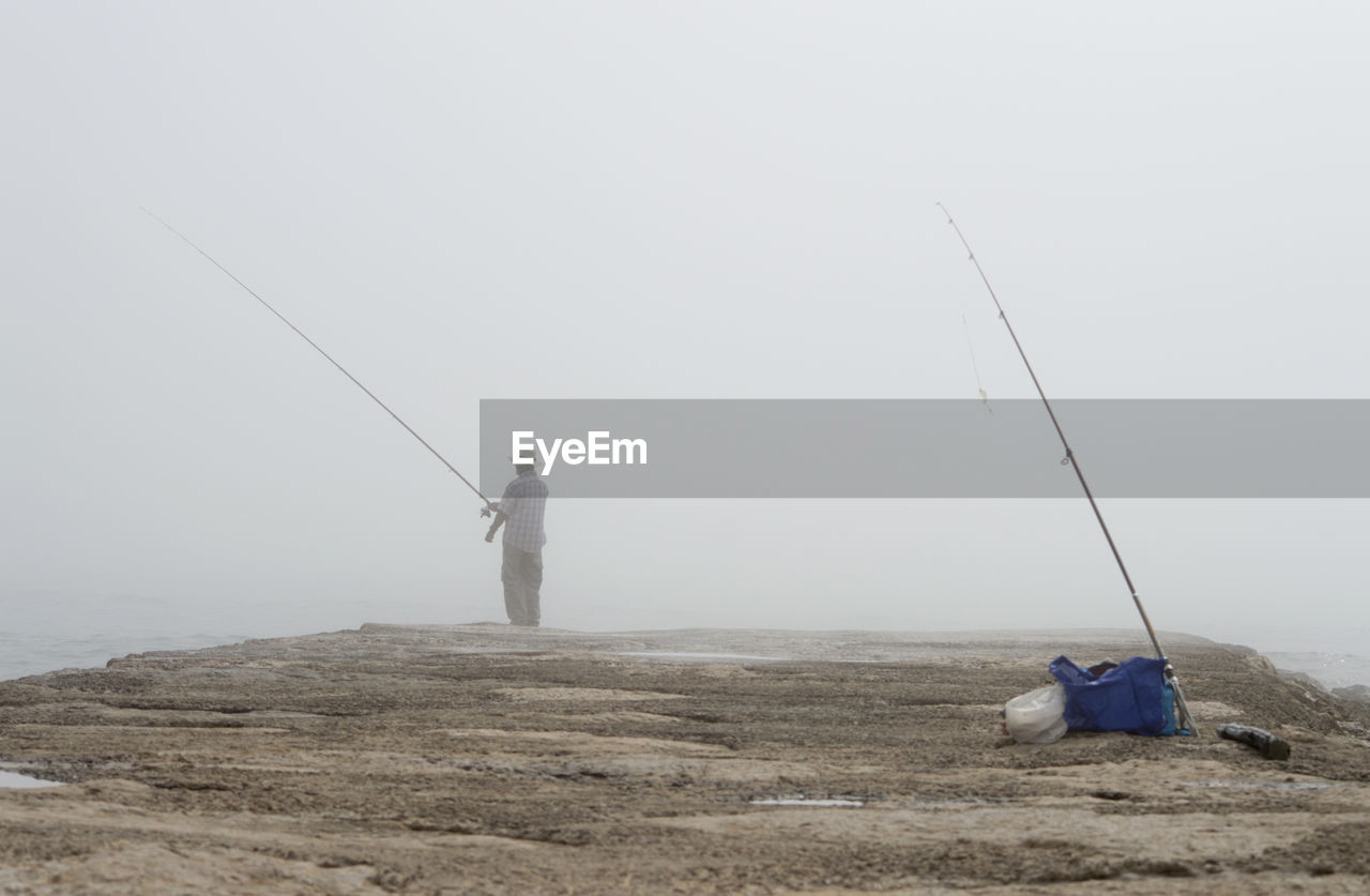 Rear view of man fishing in lake during foggy weather