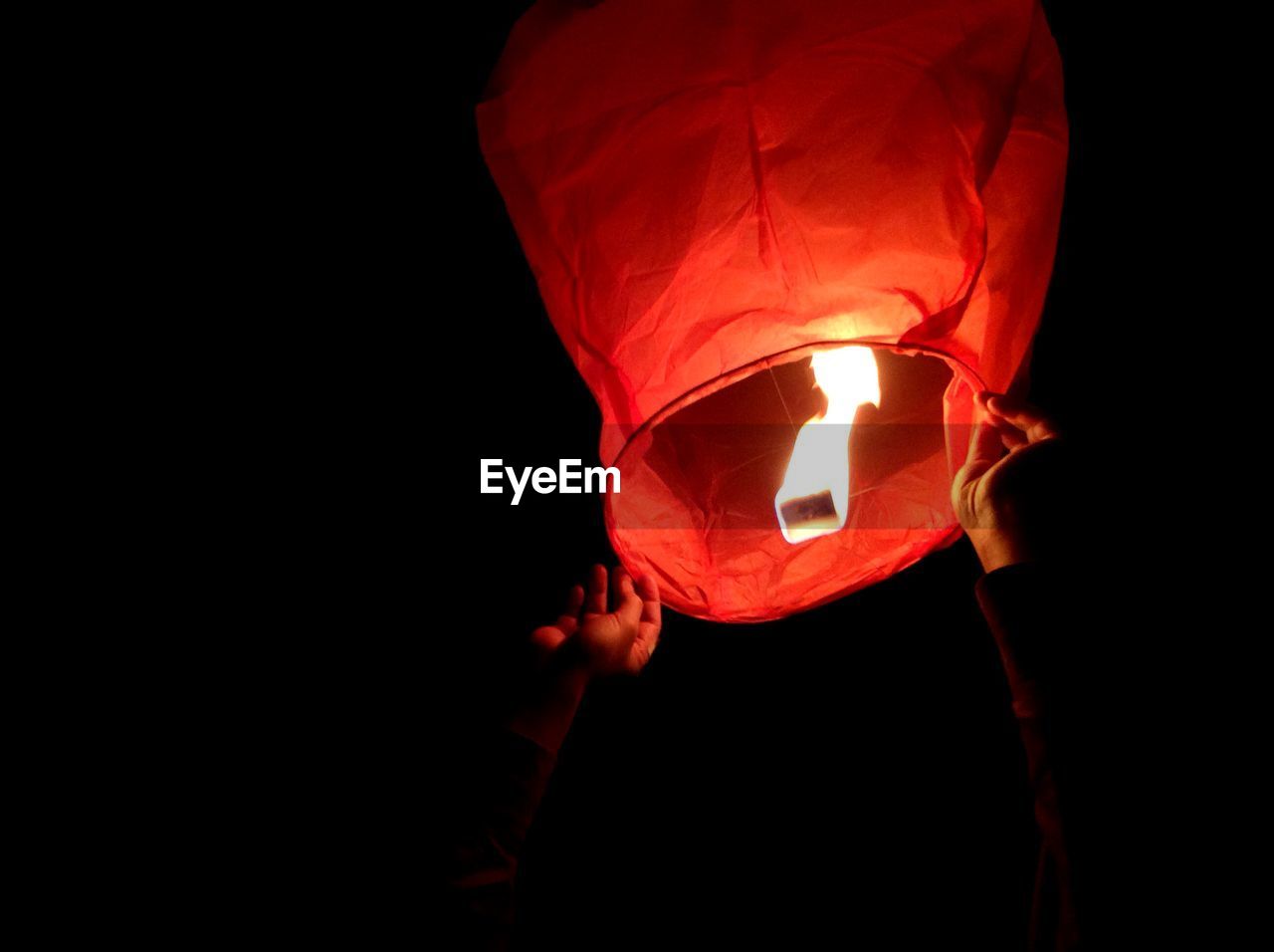 Cropped image of hands releasing lantern in sky at night