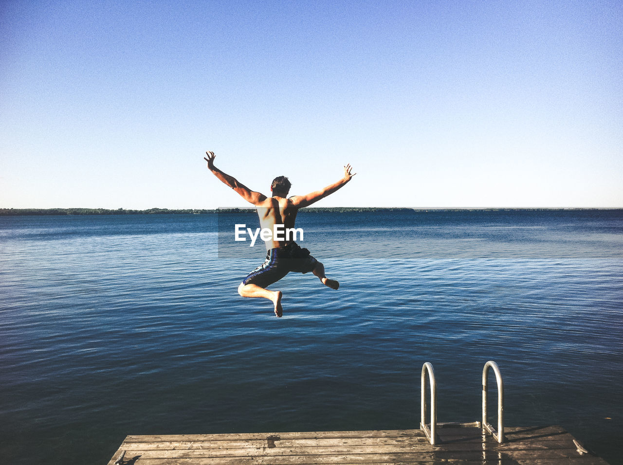 Full length of shirtless man jumping in sea against clear sky