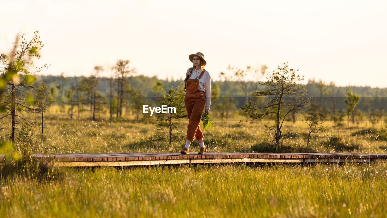 Naturalist woman exploring wildlife and ecotourism adventure walking on path through peat bog swamp.