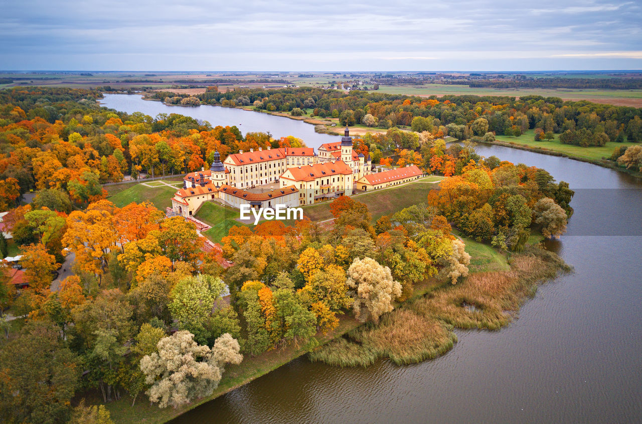 HIGH ANGLE VIEW OF RIVER BY TREES AND BUILDINGS AGAINST SKY