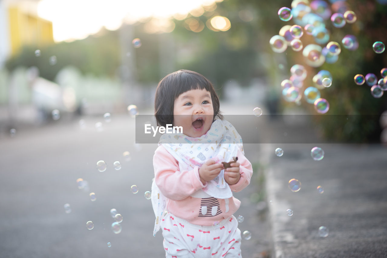 Cute girl looking at bubbles while standing on road