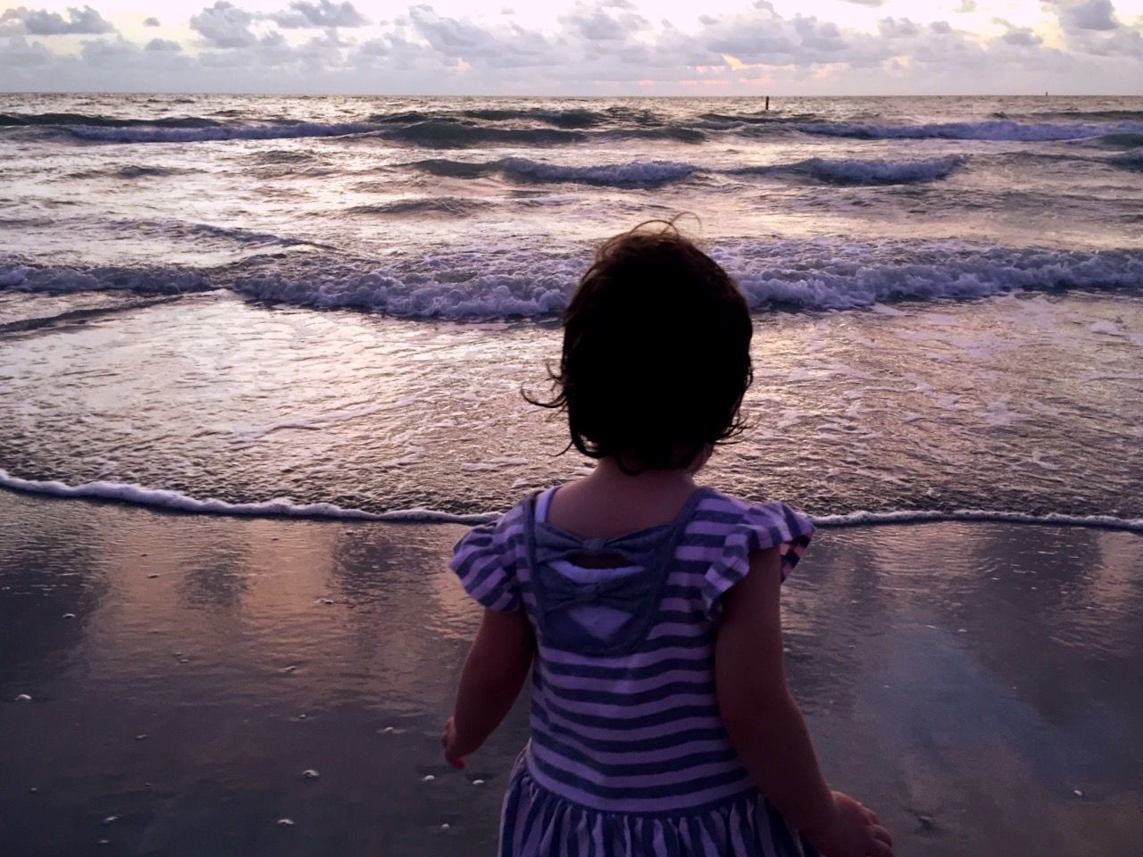 Rear view of girl standing on beach against sky during sunset