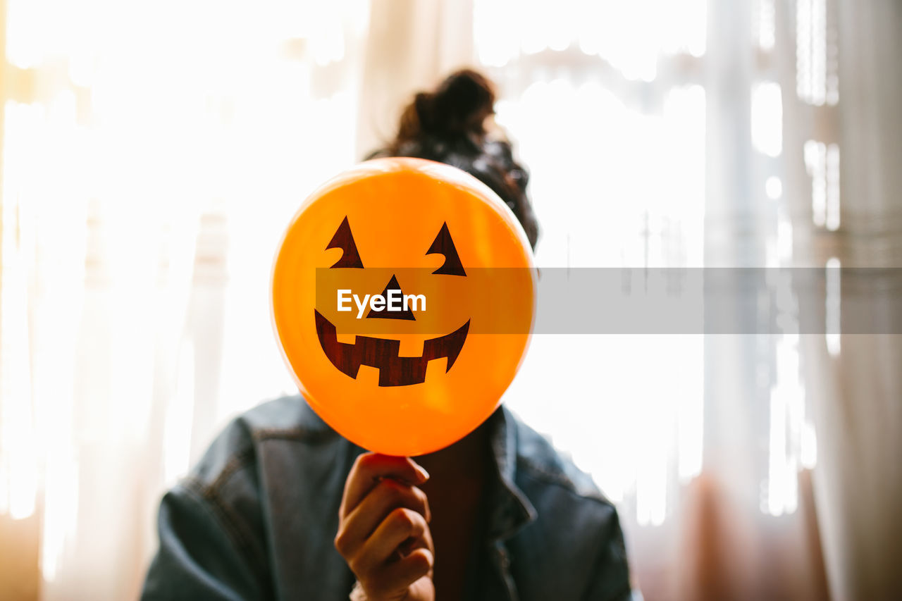 Close-up of woman holding halloween decoration against face at home