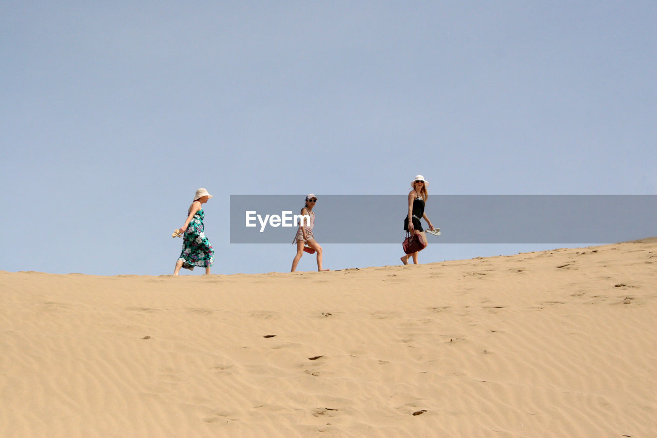 Low angle view of family walking at beach against clear sky