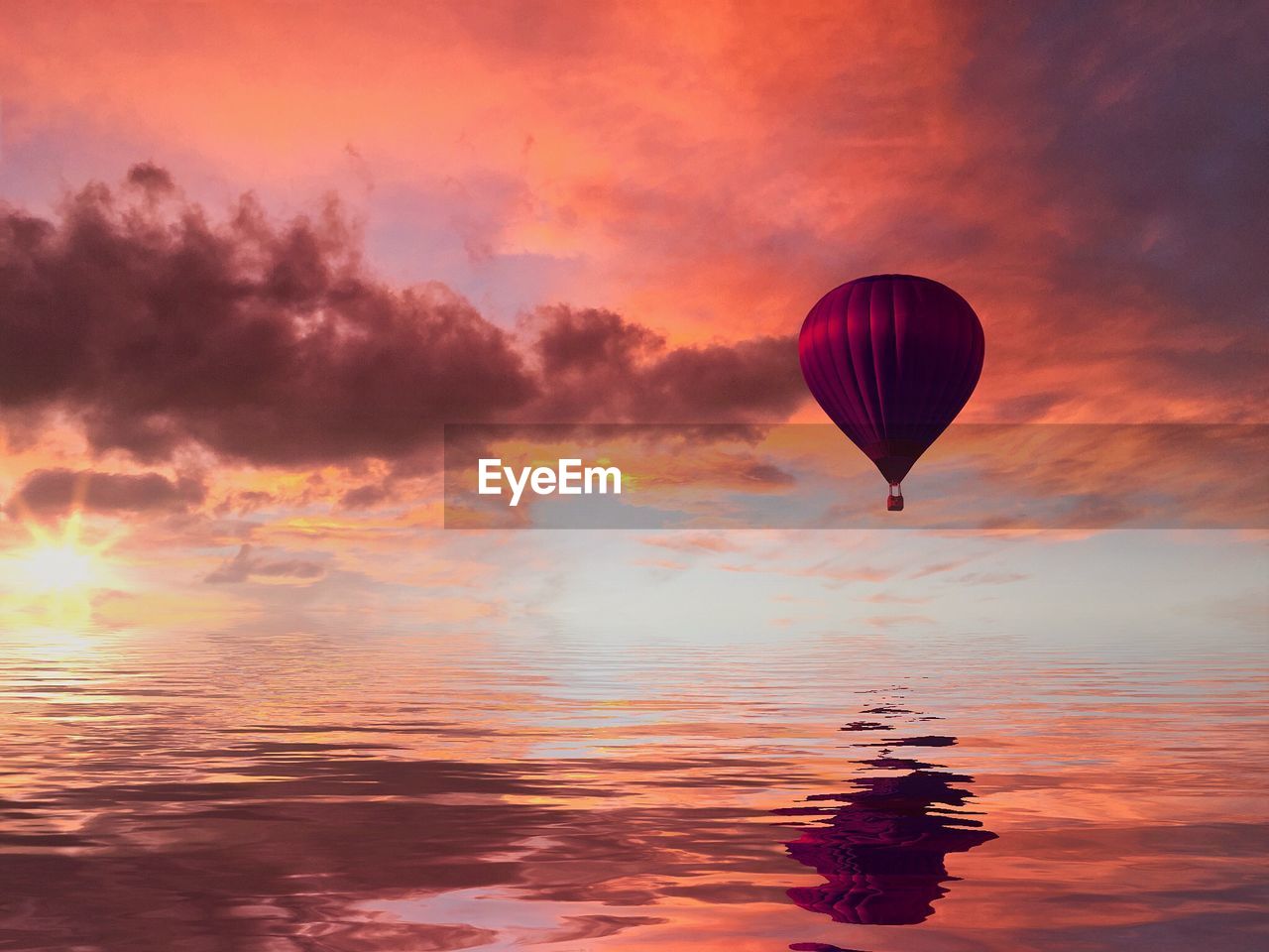 Hot air balloon flying over sea against cloudy sky during sunset