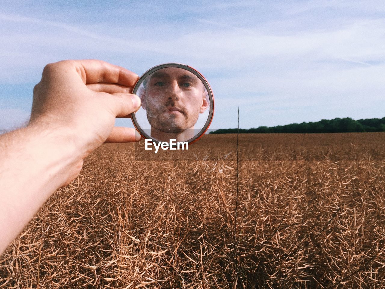 Close-up of man's reflection in mirror against wheat field