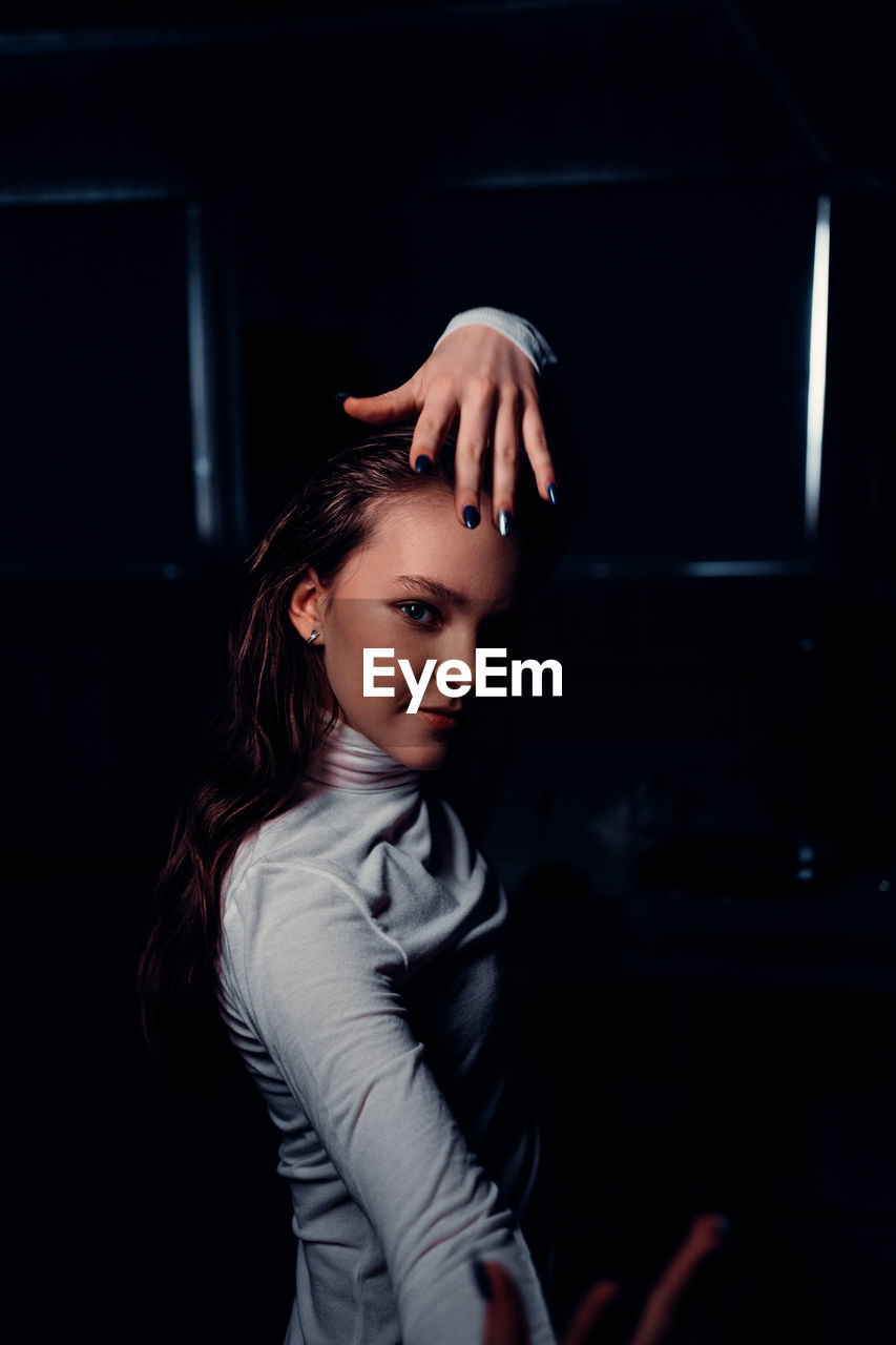 Portrait of woman standing against dark room