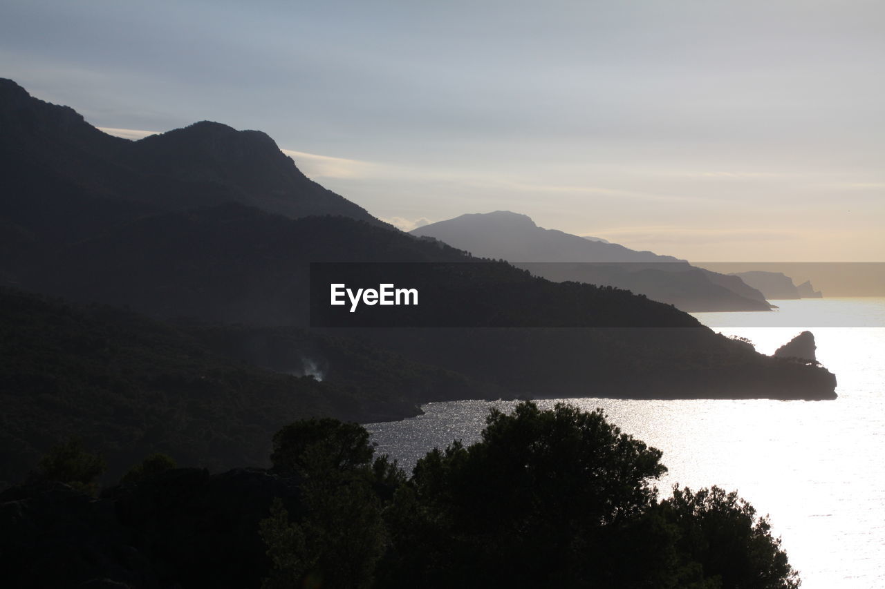 Silhouette mountains by sea against sky during sunset