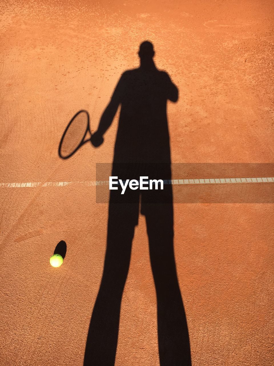 Shadow of man holding tennis racket and standing at court 