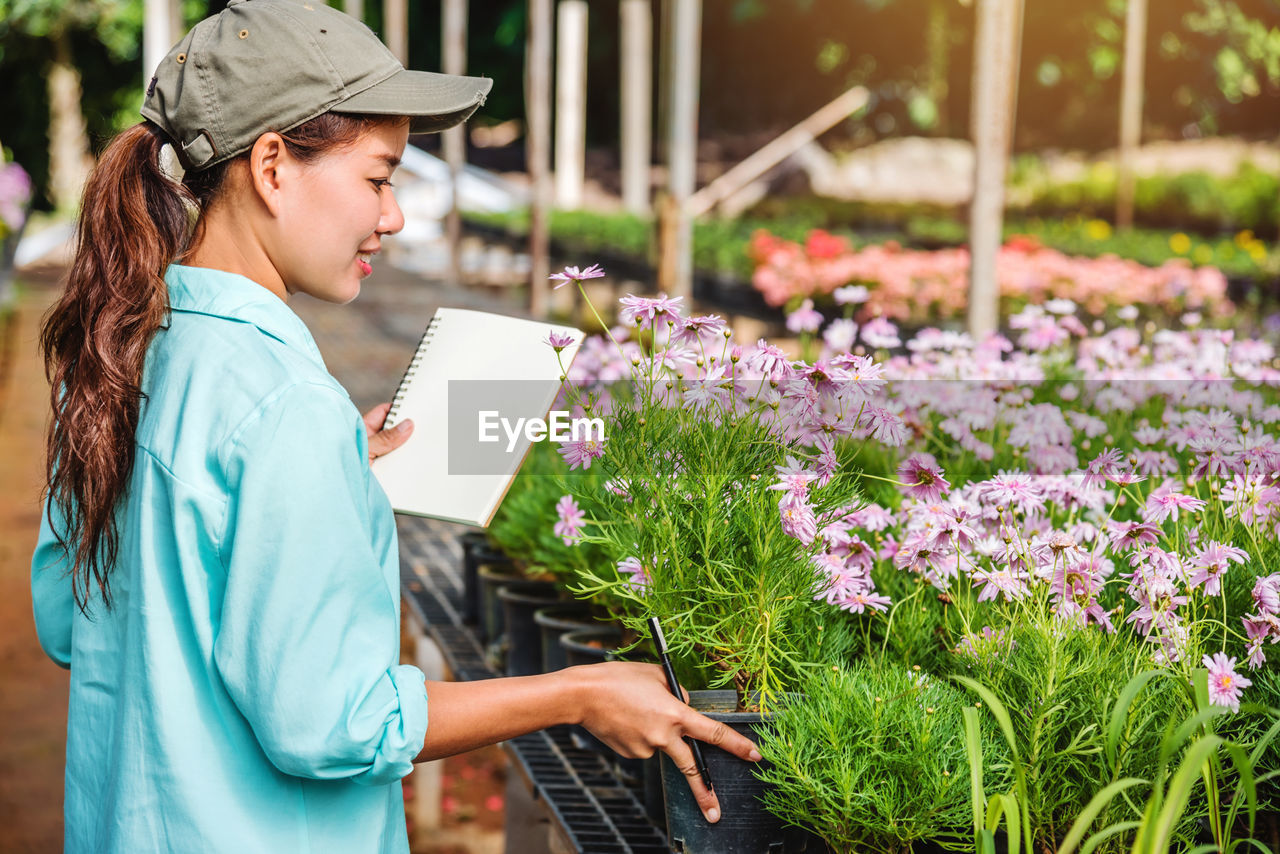 SIDE VIEW OF WOMAN LOOKING AT FLOWERING PLANT